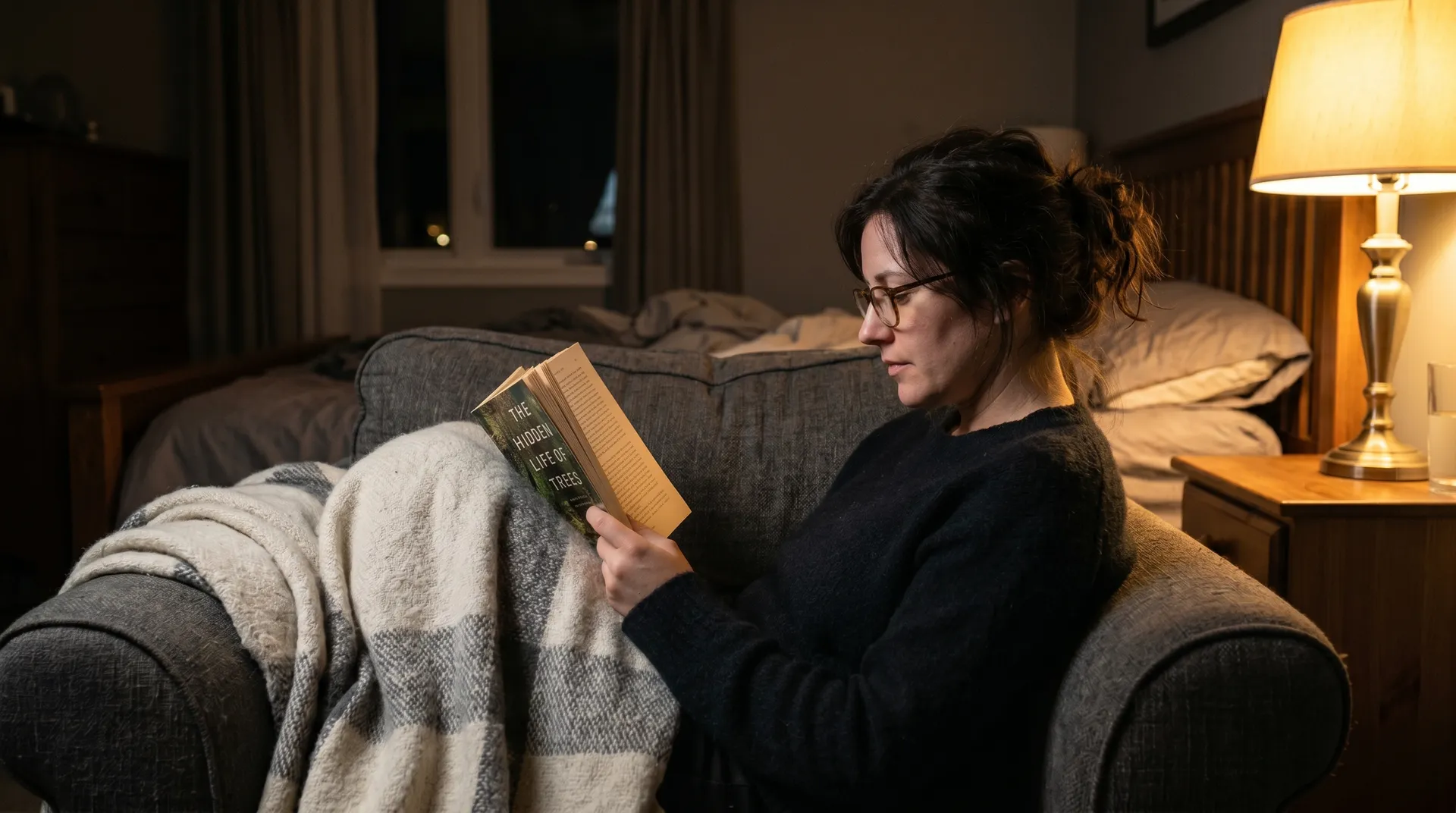 Person som läser bok i fåtölj med skön belysning istället för att ligga vaken i sängen